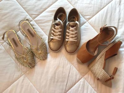 Step three of the travel packing capsule wardrobe is to add three pairs of shoes. Image shows a pair of sneakers, espadrilles and flat heeled, brushed gold sandals.