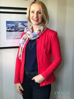 Women wears deep blue top and jeans, coral jacket and multi-coloured scarf.