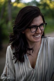 Woman with black hair wears complementary black framed glasses.