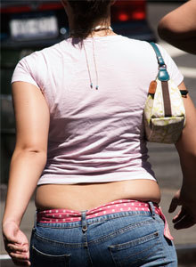 Woman wears jeans that are too tight exposing rolls of fat that hang over the top of the jeans.