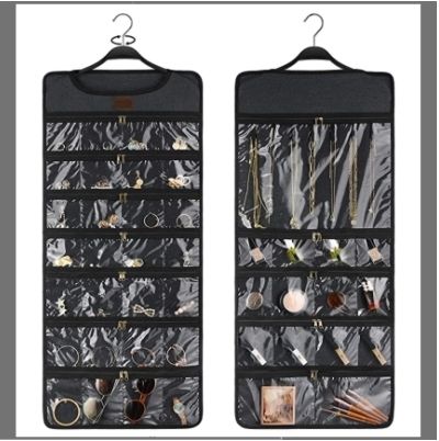 A charcoal coloured hanging jewellery holder is filled with necklaces, bangles, earrings, sunglasses, and makeup.
