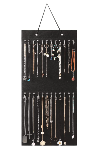 A black felt necklace holder hangs on a wall. There is one necklace hanging from each of the twenty-four hooks.