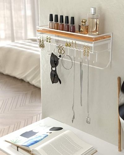 A white jewellery organiser is attached to a bedroom wall. It has earrings, necklaces and sunglasses hanging on the hooks.