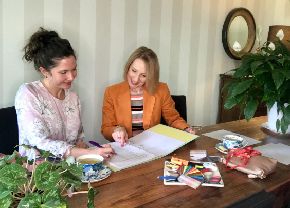 Two women looking at a folder which is filled with style information. They are sitting next to each other at a wooden table. The lady in the mauve shirt is enjoying a Personal Style consultation with Ann Vodicka in Sydney.