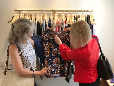 Two women in a fashion store looking at a patterned tee shirt. Ann Vodicka is personal shopping with her client.