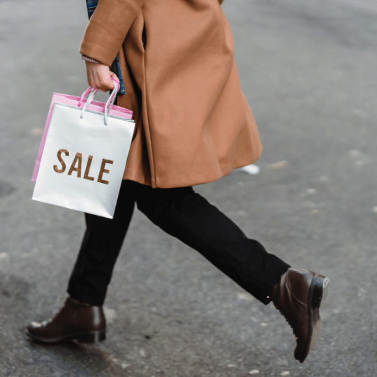 A woman is wearing a winter coat and carrying two 'Sale' bags.