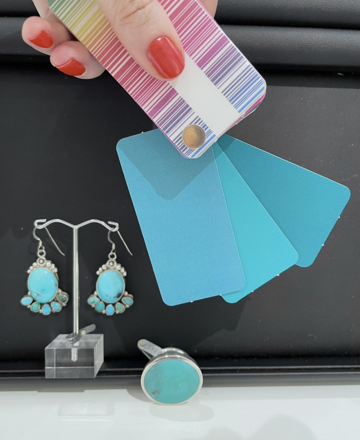 A person is holding her colour swatch to show how the turquoise earrings and ring matches her personal colour palette.