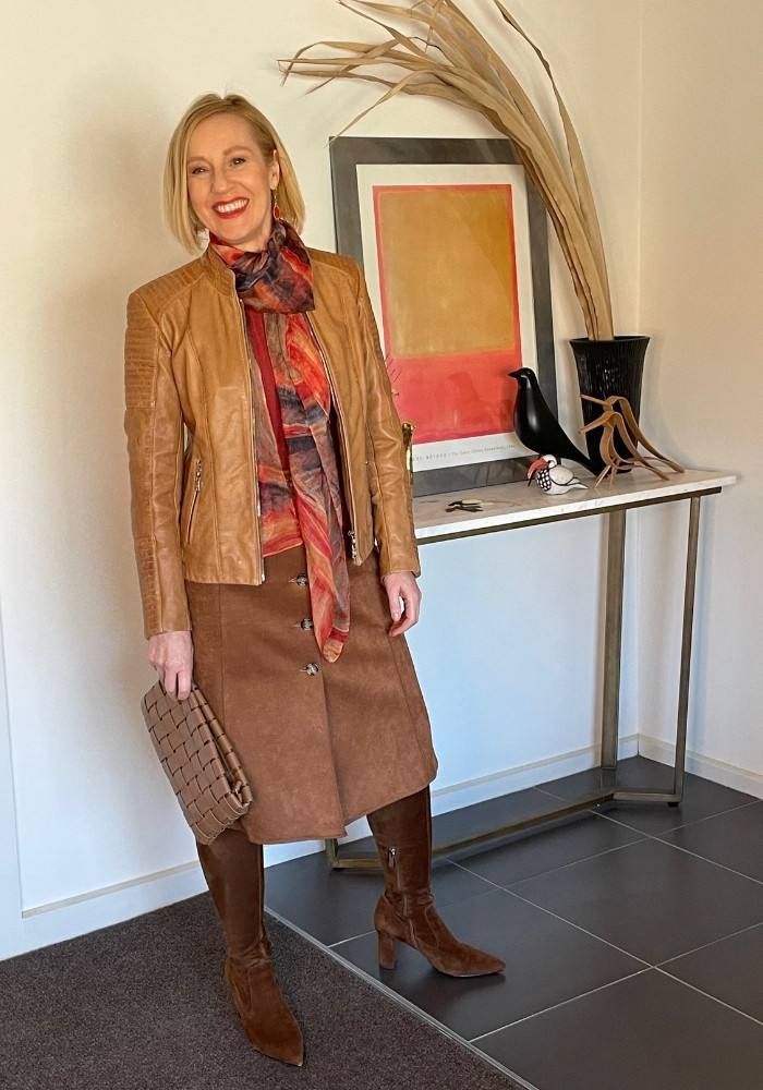 A woman is wearing a brown skirt and boots with a red scarf.